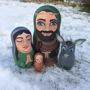 May include: Hand-painted wooden nesting dolls depicting the Nativity scene. The set includes Joseph, Mary, baby Jesus, and a donkey. The dolls are painted in a traditional style with realistic features and bright colors.
