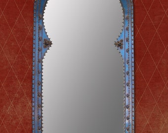 May include: An arched wall mirror featuring a blue metal frame with a scalloped inner edge. The frame is decorated with small metal studs along the perimeter and ornate gold-toned floral accents at the top, sides, and bottom center.