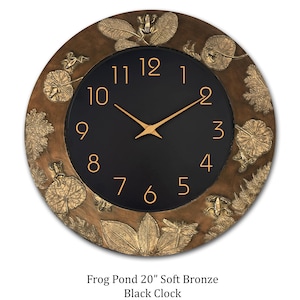 May include: A round, bronze-colored wall clock with a black face. The clock features gold-colored hands and numerals. The outer rim is decorated with embossed leaves, frogs, and dragonflies. The clock is approximately 20 inches in diameter.