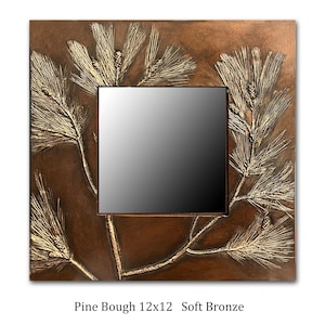 May include: A 12x12 inch soft bronze mirror with a pine bough design. The mirror has a dark brown frame with a raised pine bough design in a lighter bronze color.