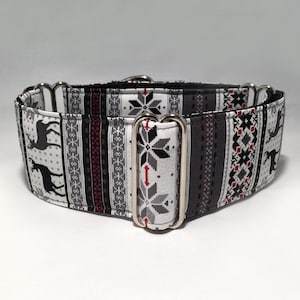 May include: A wide dog collar with a festive pattern. The fabric features a repeating design of reindeer, snowflakes, and geometric shapes in shades of gray, black, white, and red. The collar has silver-colored metal hardware.