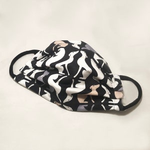 May include: A black face mask with a repeating pattern of white, gray, and tan dog silhouettes. The mask has black ear loops and is made of a pleated fabric.