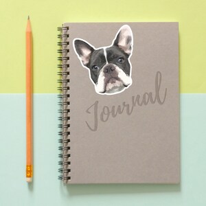 May include: A gray journal with a black and white French Bulldog sticker on the front. The journal has a spiral binding and the word "Journal" written in cursive on the front.