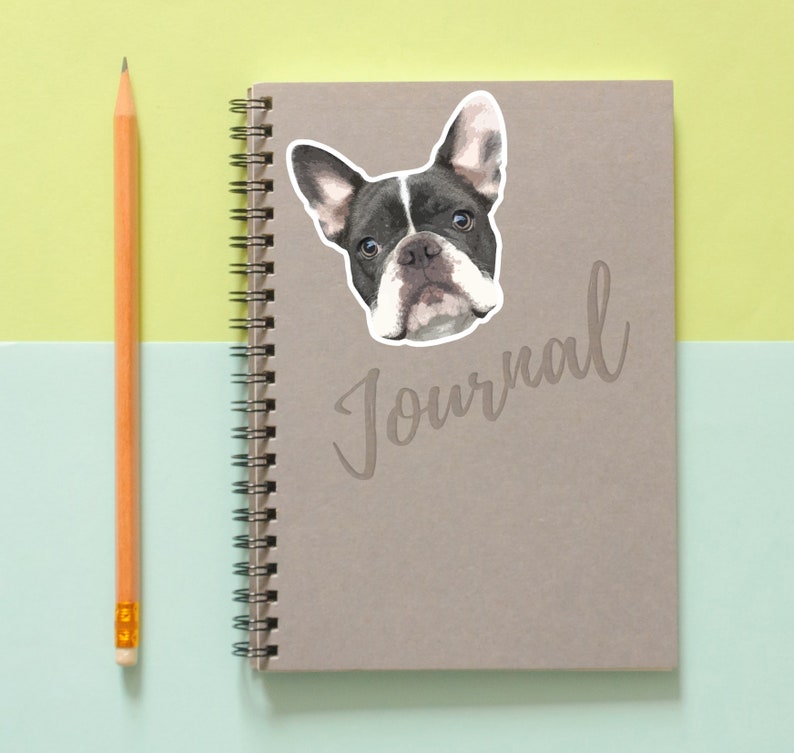 May include: A gray journal with a black and white French Bulldog sticker on the front. The journal has a spiral binding and the word "Journal" written in cursive on the front.