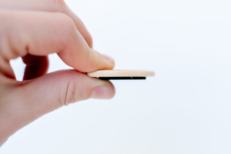 Pu&ograve; includere: Un magnete rotondo in legno con un retro magnetico nero. Il magnete &egrave; tenuto da una mano.