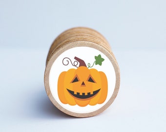 May include: A stack of round wooden craft tags with a white sticker on the top tag. The sticker features a cartoon jack-o'-lantern with a smiling face.