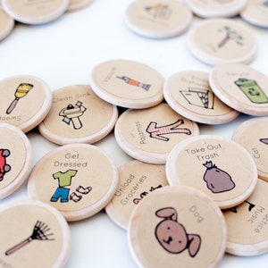 Pu&ograve; includere: Un set di 15 gettoni rotondi in legno con varie illustrazioni e testo. I gettoni presentano immagini di un gatto, un cane, un sacchetto della spazzatura, un tosaerba, una scopa, un lavandino, vestiti, pigiama, generi alimentari e un rastrello. Il testo sui gettoni include "Falciare", "Spazzare", "Vestirsi", "Pulire il lavandino", "Scaricare la spesa", "Cane", "Pigiama", "Portare fuori la spazzatura", "Gatto" e "Esercitarsi con la musica".