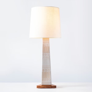 May include: A white ceramic table lamp with a white fabric lampshade. The lamp base has a geometric pattern.