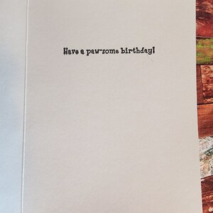 May include: A white card with the text "Have a paw-some birthday!" printed in black.
