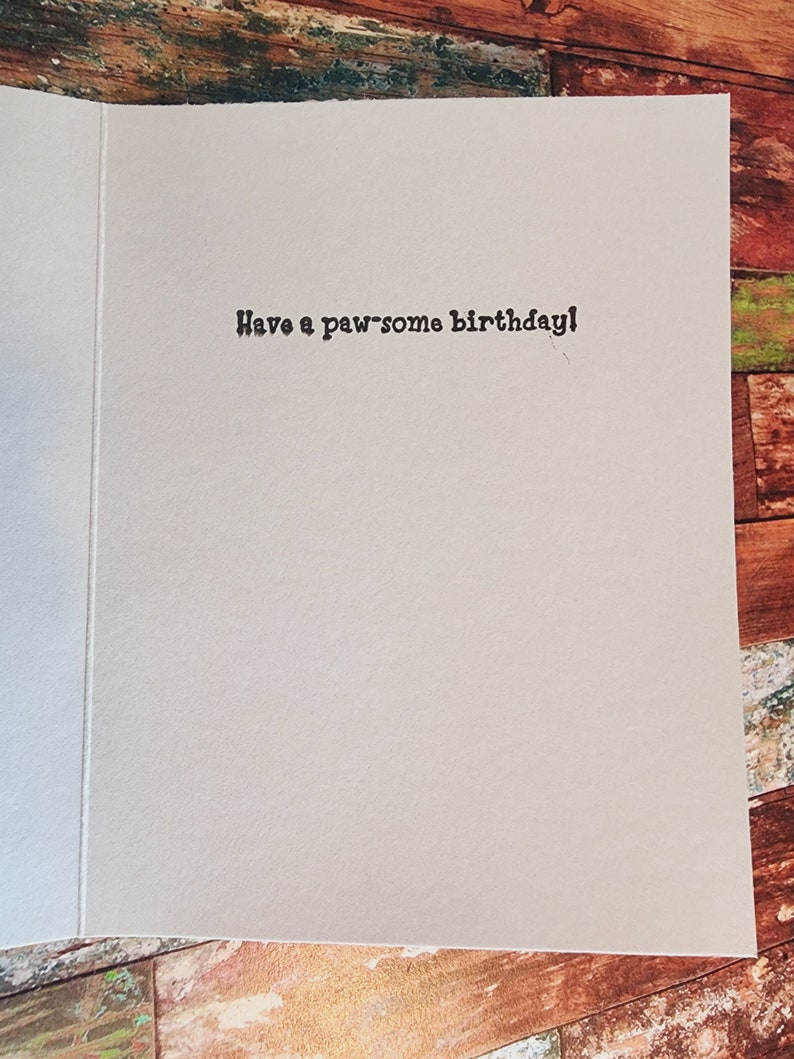 May include: A white card with the text "Have a paw-some birthday!" printed in black.