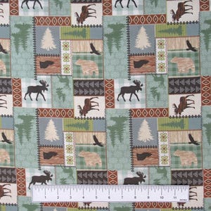 May include: A patchwork fabric with a woodland theme. The design features squares with moose, bears, eagles, and trees in shades of green, brown, and beige. The ruler at the bottom measures up to 11 inches.