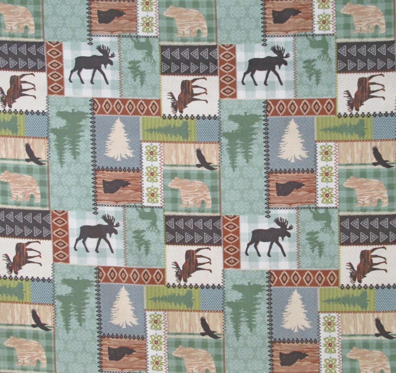 May include: A patchwork fabric with a repeating pattern of woodland creatures and nature scenes. The design features moose, bears, eagles, and trees in a palette of green, brown, and beige. Geometric shapes and decorative borders frame the images, creating a rustic, outdoorsy theme.