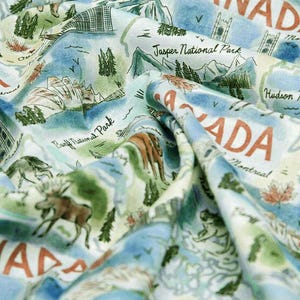 May include: A fabric with a map of Canada design. The fabric features illustrations of mountains, trees, and wildlife, with text including "Canada", "Jasper National Park", and "Banff National Park". The color palette includes shades of blue, green, and brown.