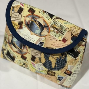 May include: A blue and beige fabric pouch with a flap closure. The pouch is decorated with a vintage travel theme, featuring images of maps, globes, airplanes, and postage stamps. The text "Carte Postale" is visible on the pouch.