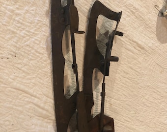 May include: A pair of antique ice skates with a leather strap. The skates are made of metal and have a rusty patina. The skates are attached to a leather strap that is worn and faded.