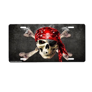 May include: A black and white skull with a red bandana and an eye patch, with crossed bones behind it. The skull is on a black background with a white border.