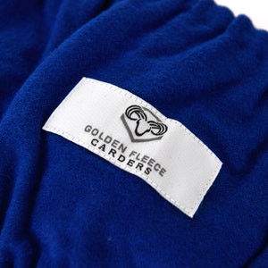 May include: A white label with black text and a ram logo reads "Golden Fleece Carders". The label is sewn onto a royal blue fabric.