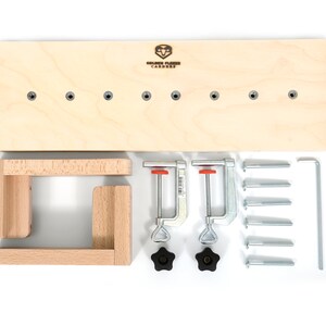 May include: A wooden woodworking jig kit with a wooden base, two clamps, eight screws, two knobs, and a metal tool. The base has eight holes and the text "Golden Fleece Carpentry" is printed on the base.