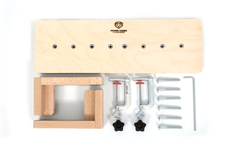 May include: A wooden woodworking jig kit with a wooden base, two clamps, eight screws, two knobs, and a metal tool. The base has eight holes and the text "Golden Fleece Carpentry" is printed on the base.