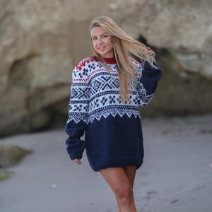 Puede incluir: Un suéter azul marino y blanco estampado con detalles en rojo. El suéter presenta un diseño geométrico en la parte superior y las mangas. El suéter es de corte holgado y parece estar hecho de un material de punto grueso.