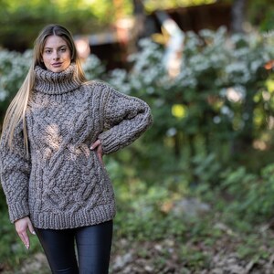 May include: A brown cable knit turtleneck sweater with a loose fit. The sweater is made of a thick, chunky yarn and has a relaxed, casual style.