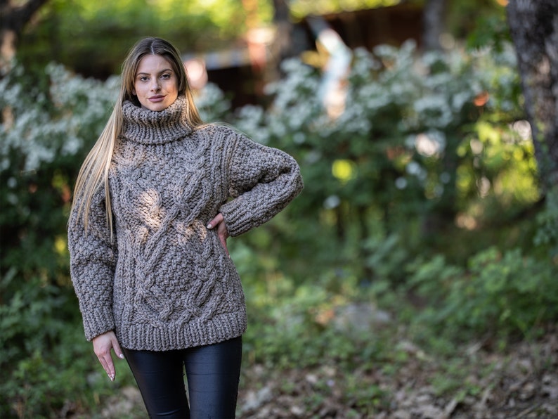 May include: A brown cable knit turtleneck sweater with a loose fit. The sweater is made of a thick, chunky yarn and has a relaxed, casual style.