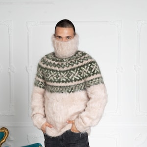 Puede incluir: Un suéter de manga larga y textura difusa en color beige claro con una cubierta de cuello integrada que llega hasta la nariz. El pecho y los hombros presentan un patrón geométrico en verde oscuro y beige con un acabado similar al mohair.