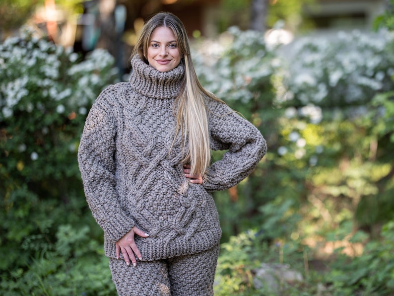 May include: A brown cable knit sweater and matching pants. The sweater has a high turtleneck and a loose fit.