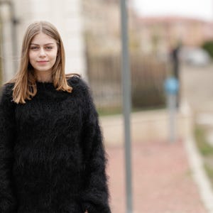 Könnte beinhalten: Ein schwarzer Langarmpullover mit einer flauschigen, strukturierten Strickoberfläche. Das Kleidungsstück hat einen Rundhalsausschnitt und eine lockere, entspannte Passform, gefertigt aus einem weichen, haarigen Material mit voluminöser Optik.