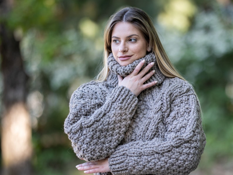May include: A close-up of a woman wearing a brown chunky knit turtleneck sweater. The sweater has a cable knit pattern and is made of a soft, warm material.