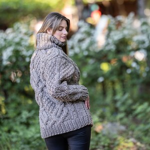 May include: A brown cable knit sweater with a turtleneck collar. The sweater is made of a thick yarn and has a loose fit.