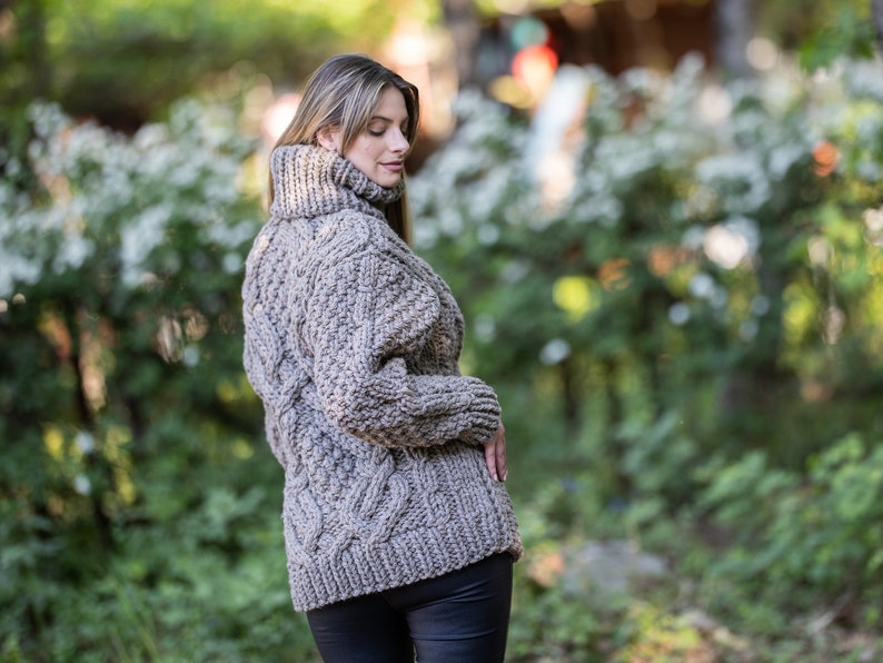 May include: A brown cable knit sweater with a turtleneck collar. The sweater is made of a thick yarn and has a loose fit.