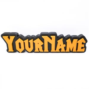 May include: A custom name sign featuring the word "YOURNAME" in a striking, orange font with a black outline. The sign is set against a white backdrop. This decorative item is likely for display.