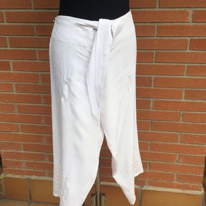 May include: White wrap skirt with a tie at the waist and embroidered floral details.
