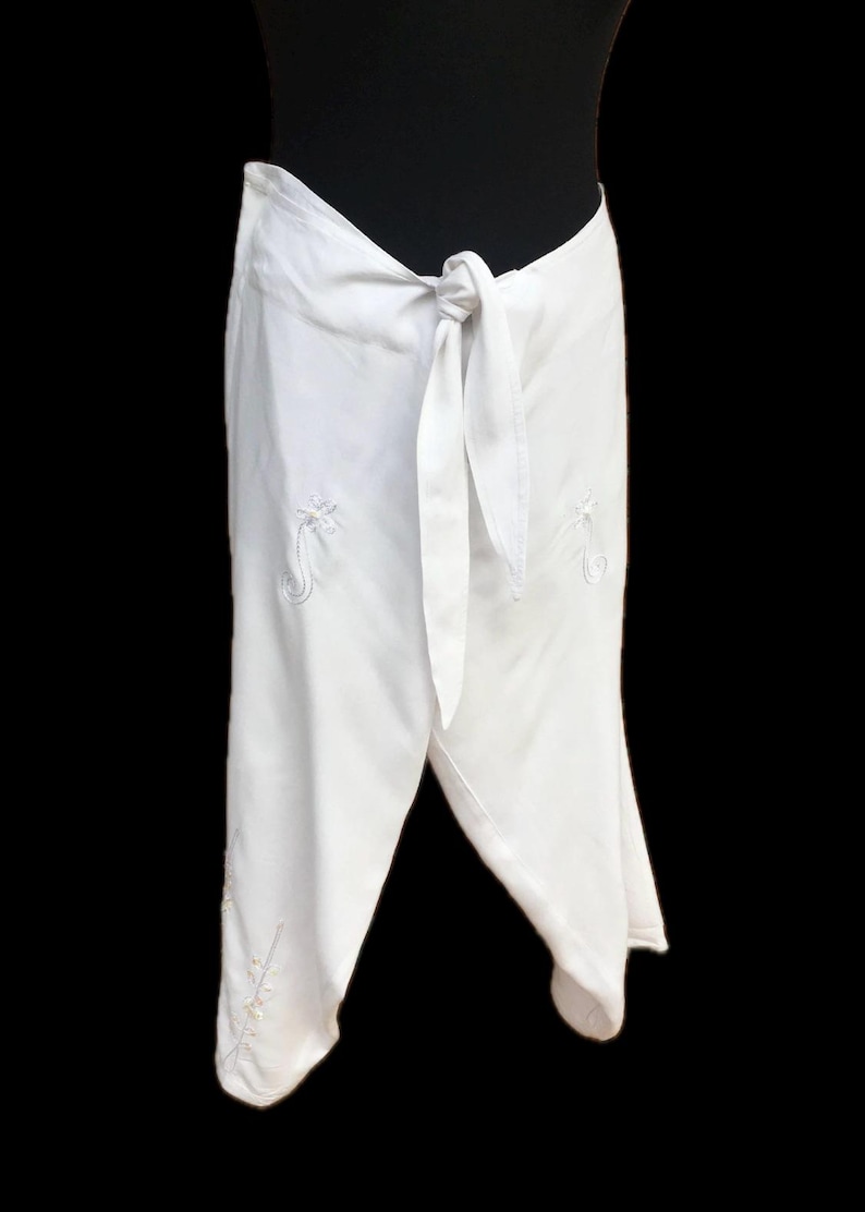 May include: White wrap skirt with a tie at the waist and embroidered floral designs.