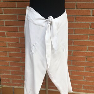 May include: White wrap pants with a tie at the waist and embroidered floral designs.