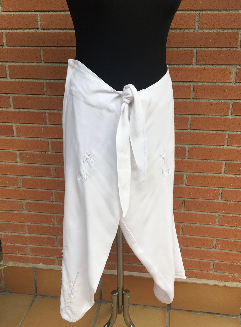 May include: White wrap pants with a tie at the waist and embroidered floral designs.