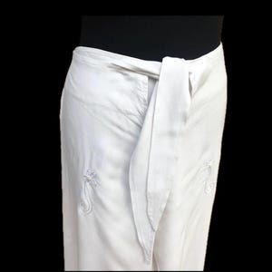 May include: White wrap skirt with a long tie and embroidered floral designs.