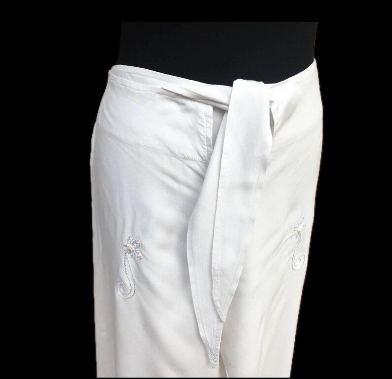 May include: White wrap skirt with a long tie and embroidered floral designs.