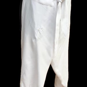 May include: White wrap pants with embroidered floral designs. The pants have a tie closure at the waist.