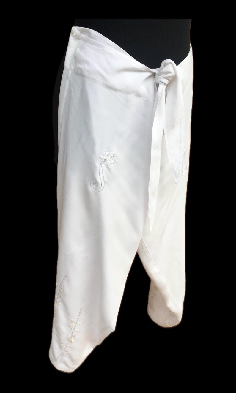 May include: White wrap pants with embroidered floral designs. The pants have a tie closure at the waist.