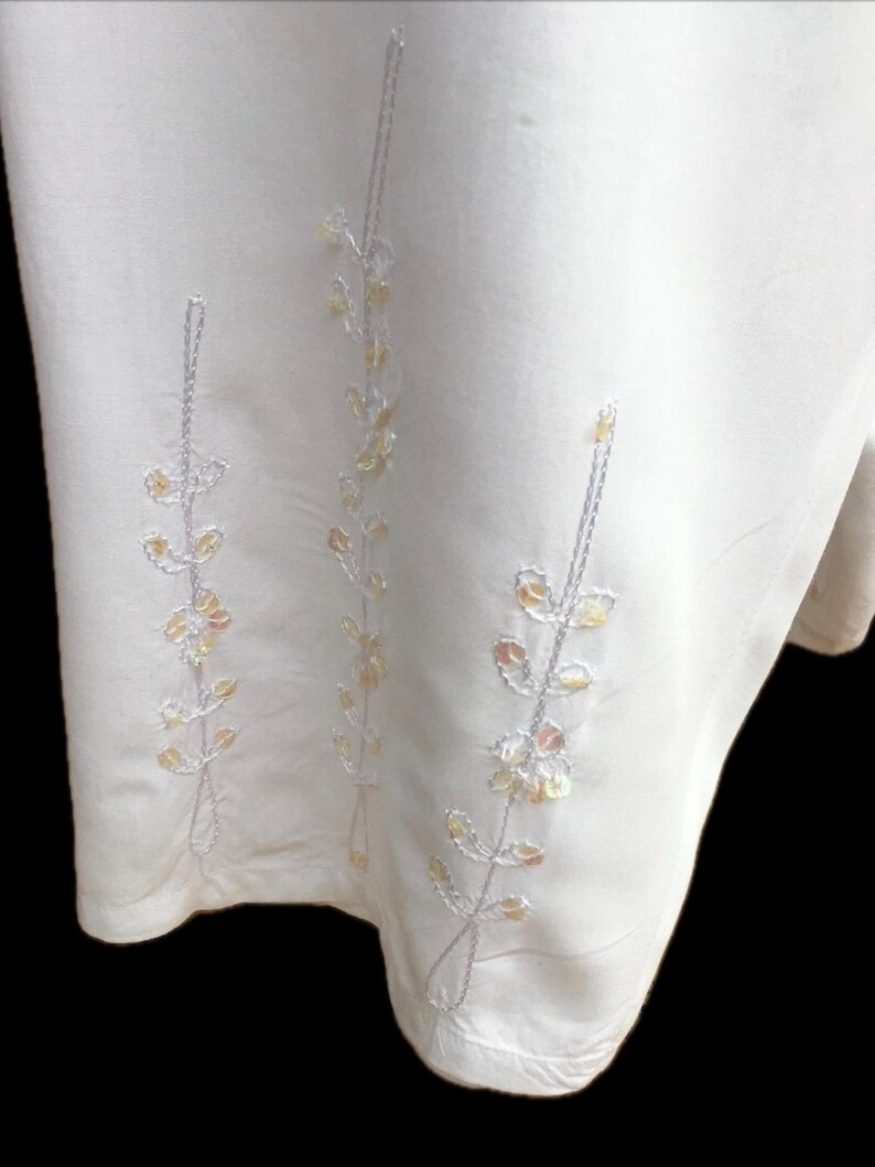 May include: White skirt with embroidered floral design featuring silver and gold sequins.