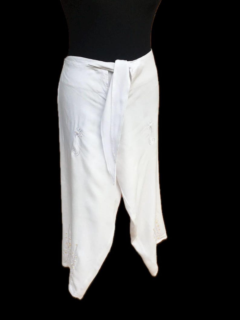 May include: White wrap skirt with a tie at the waist and embroidered details.