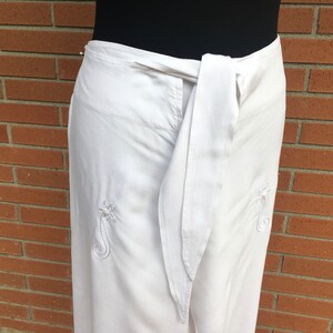 May include: White wrap pants with a white sash and embroidered floral designs.