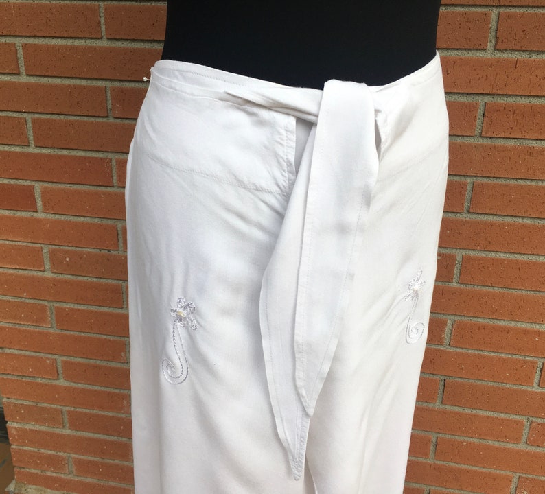 May include: White wrap pants with a white sash and embroidered floral designs.