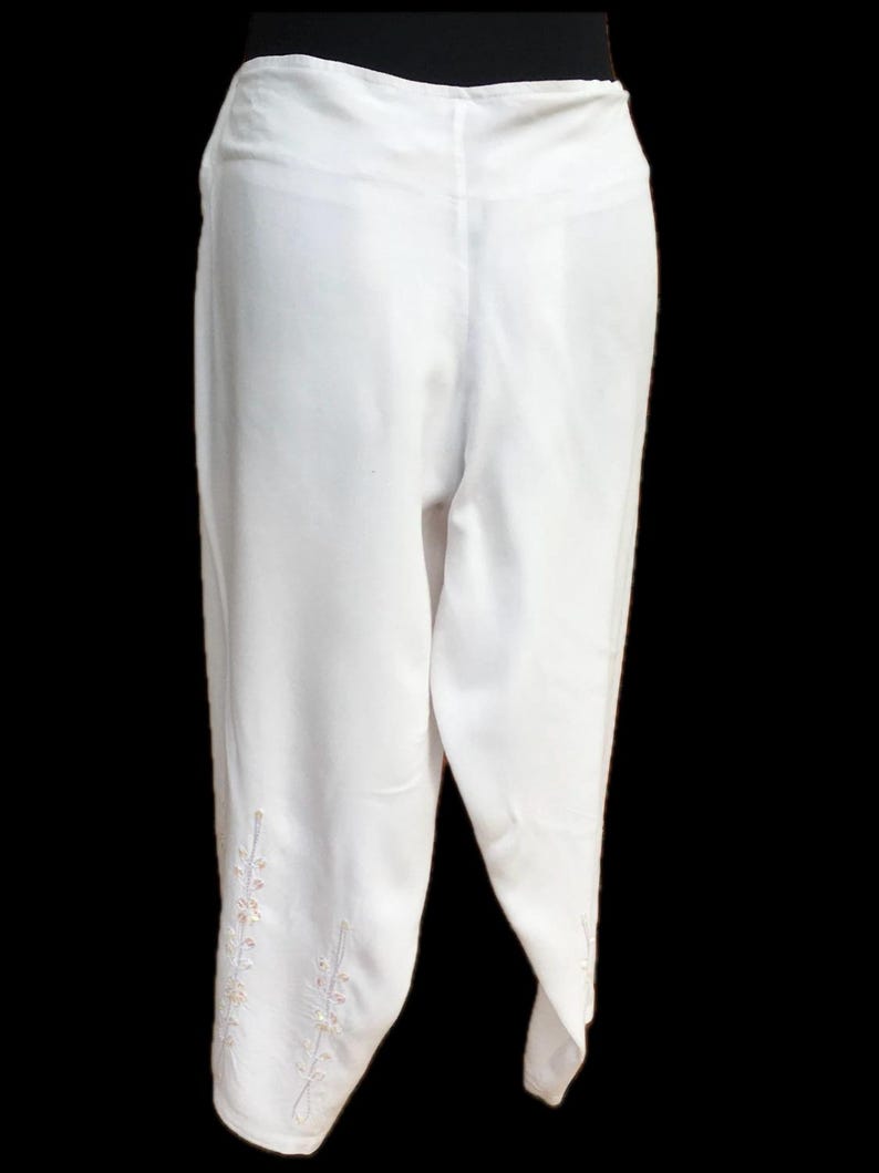 May include: White pants with a wide leg and embroidered details on the bottom.