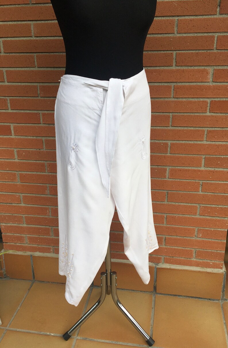 May include: White wrap skirt with a tie at the waist and embroidered floral details.