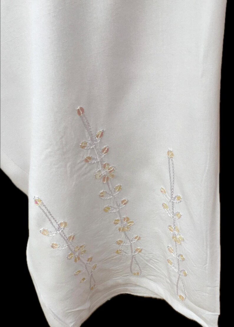 May include: White fabric with embroidered floral designs in shades of pink and yellow.