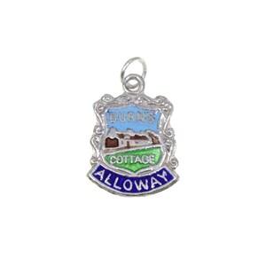 May include: A silver-toned charm with a shield-shaped design. The charm features a blue sky, a brown cottage, and green grass, with the words "Burns Cottage" and "Alloway" in blue lettering. The charm has a small loop at the top.