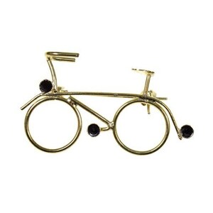 May include: A gold-coloured bicycle brooch with black accents. The bicycle design features two large circular wheels, a seat, handlebars, and a decorative frame. The brooch has three black jewels and is set against a white background.